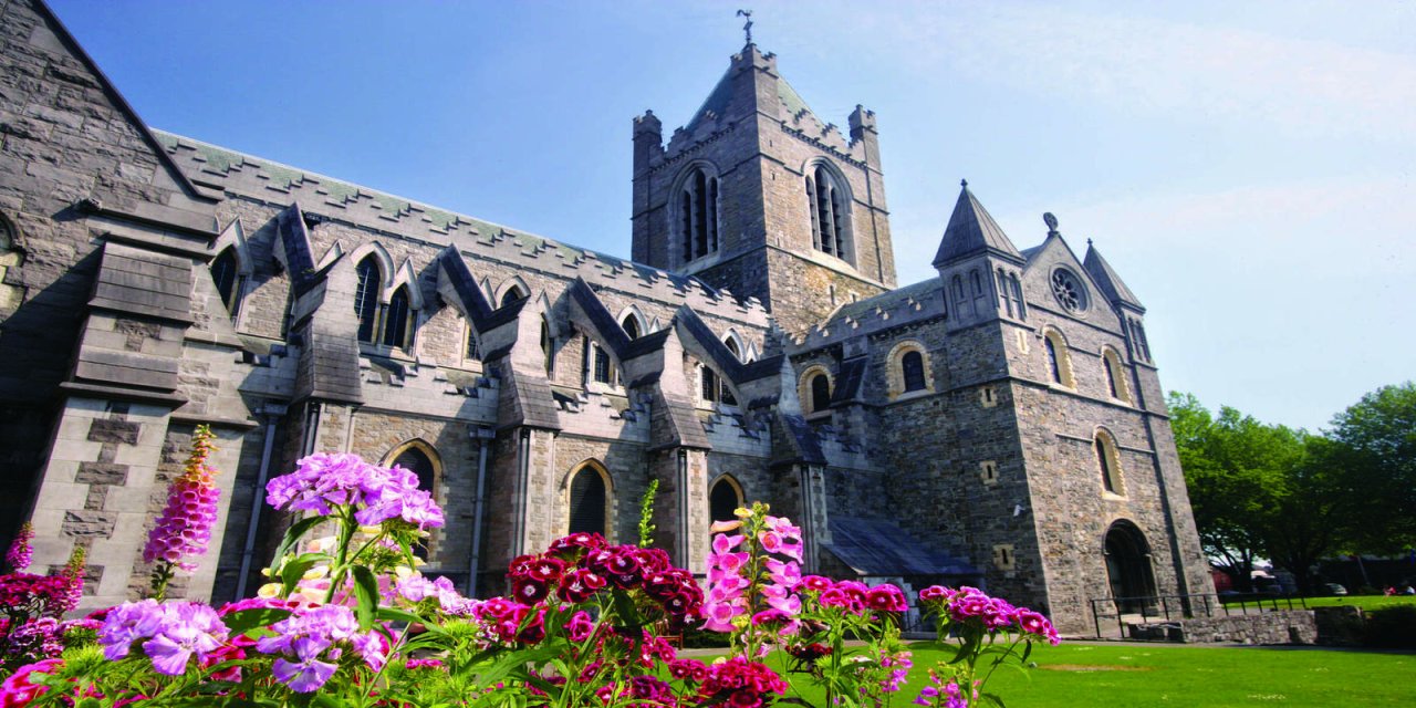 Angled view of brick grey castle surrounded by vibrant coloured pink and purple flowers sitting on a bed of bright green grass
